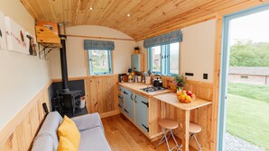 A cozy cabin interior with a wooden ceiling, a kitchenette, a sofa with cushions, and a view of the outdoors. - Victoria Hut near Allerford (Allerford)