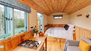 A cozy bedroom with a wooden ceiling, a bed with white bedding, a small bedside table, and a window with a view of greenery. - Victoria Hut near Allerford (Allerford)