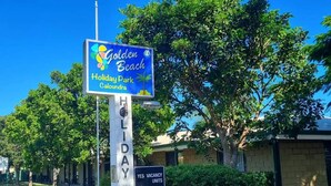A sign for Golden Beach Holiday Park with a clear view of the surrounding greenery and a building in the background. - Golden Beach Holiday Park (Golden Beach)