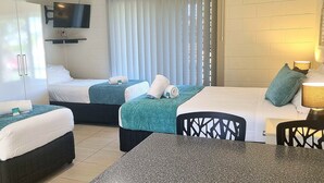 A hotel room with two beds, a TV mounted on the wall, a table with chairs, and a window with blinds. - Golden Beach Holiday Park (Golden Beach)