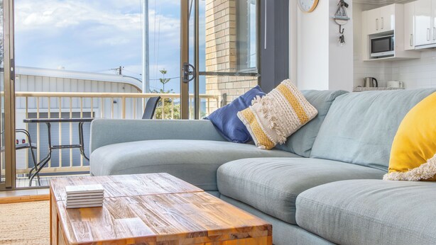 A modern living room with a grey sofa, wooden coffee table, and a view of a building through a glass door.