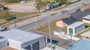 An aerial view of a coastal area with a beach, a road, and industrial buildings.