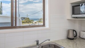 A kitchen with white cabinets, a stainless steel sink, a kettle, and a microwave.