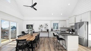 Een ruime keuken met een centraal eiland, witte kasten en een eethoek met een houten tafel en stoelen.