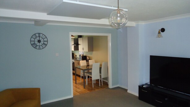 Una sala de estar con un televisor de pantalla plana, un comedor con mesa y sillas, y una cocina al fondo.