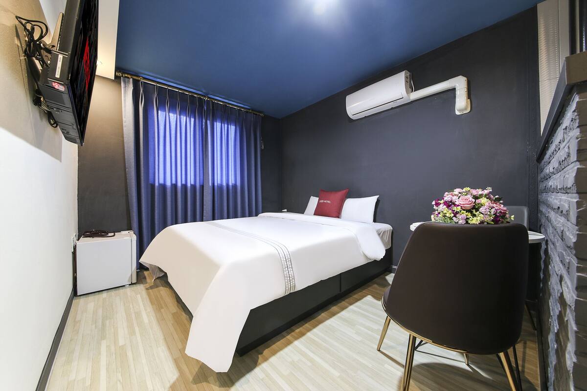 Ein modernes Hotelzimmer mit einem großen Bett, einem kleinen Nachttisch, einem Sessel und einer Wand-Klimaanlage.