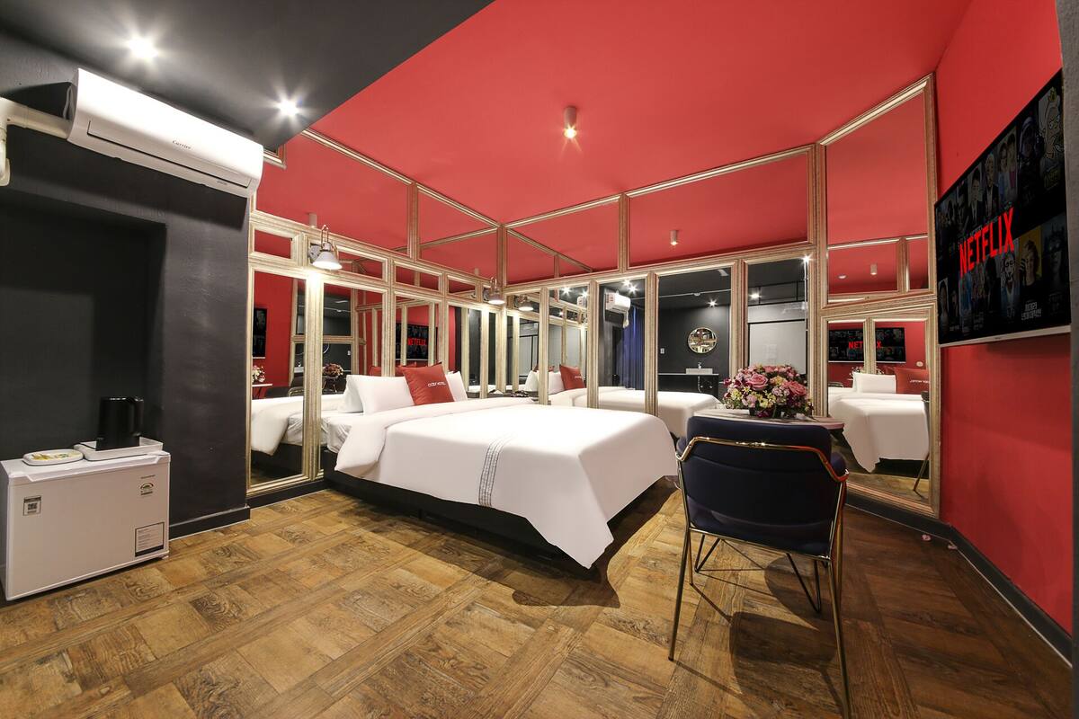Ein modernes Hotelzimmer mit einem großen Bett, einem Schreibtisch und einem Stuhl. Mehrere Spiegel sind an den Wänden angebracht, und ein Fernseher ist an der Wand befestigt.