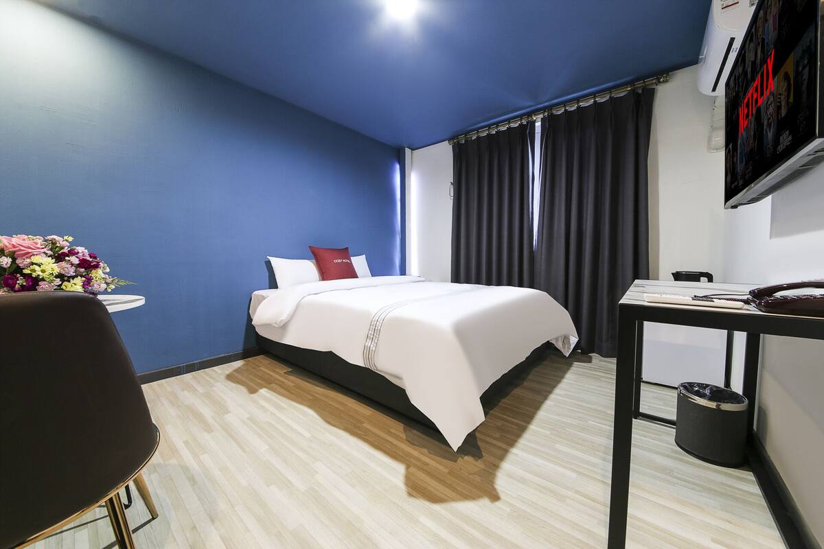 Ein Hotelzimmer mit Bett, Schreibtisch, Stuhl, Fernseher und einem Fenster mit Vorhängen.