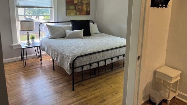 Un dormitorio con cama, ventana, lámpara y estante fijado a la pared.