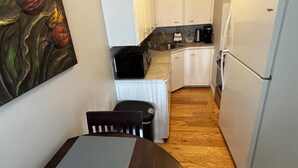 Una cocina compacta con armarios blancos, un refrigerador, un lavamanos y una cafetera.