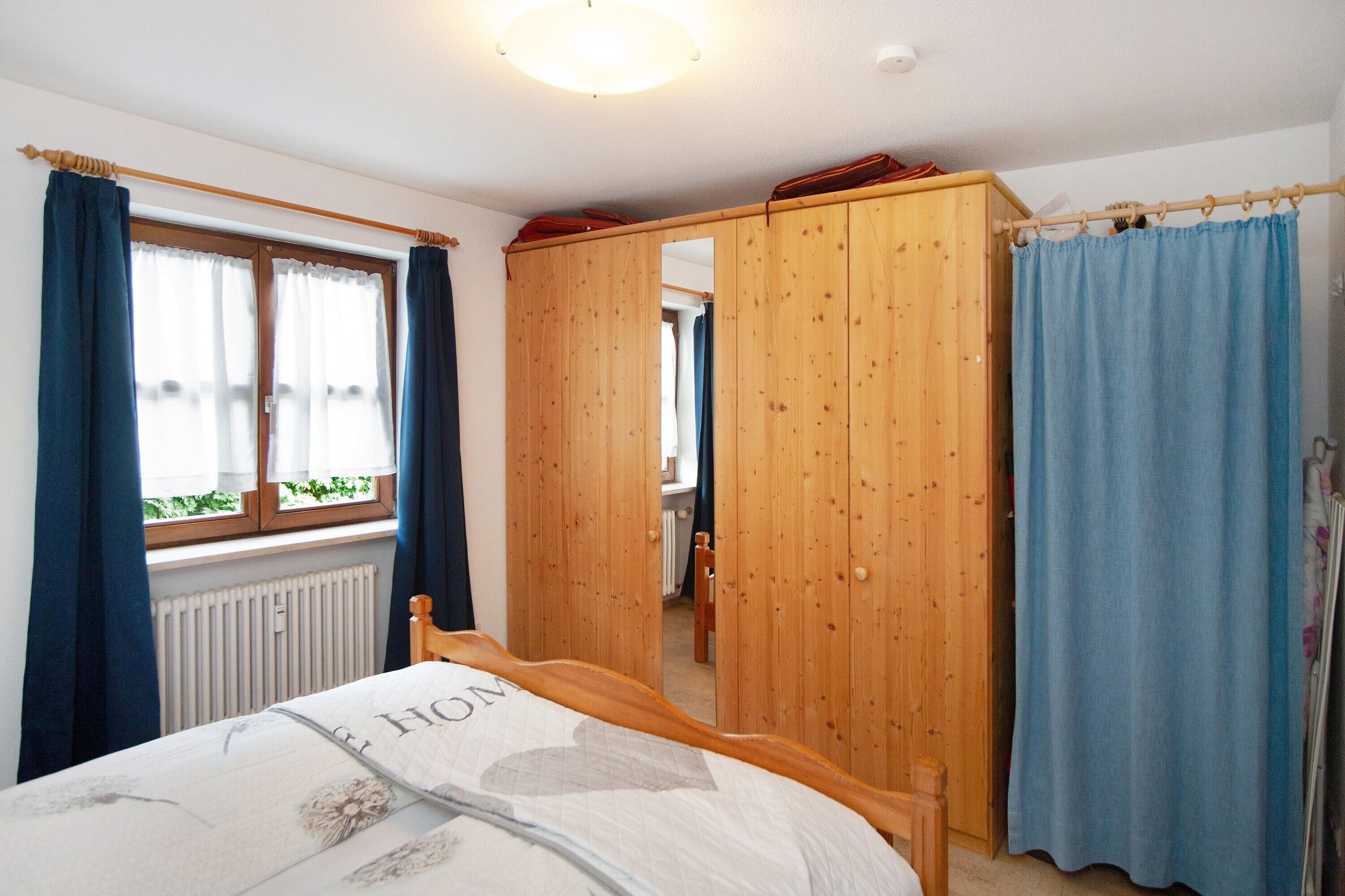 Ein Schlafzimmer mit Bett, Holzschrank und einem fenster mit Vorhängen.