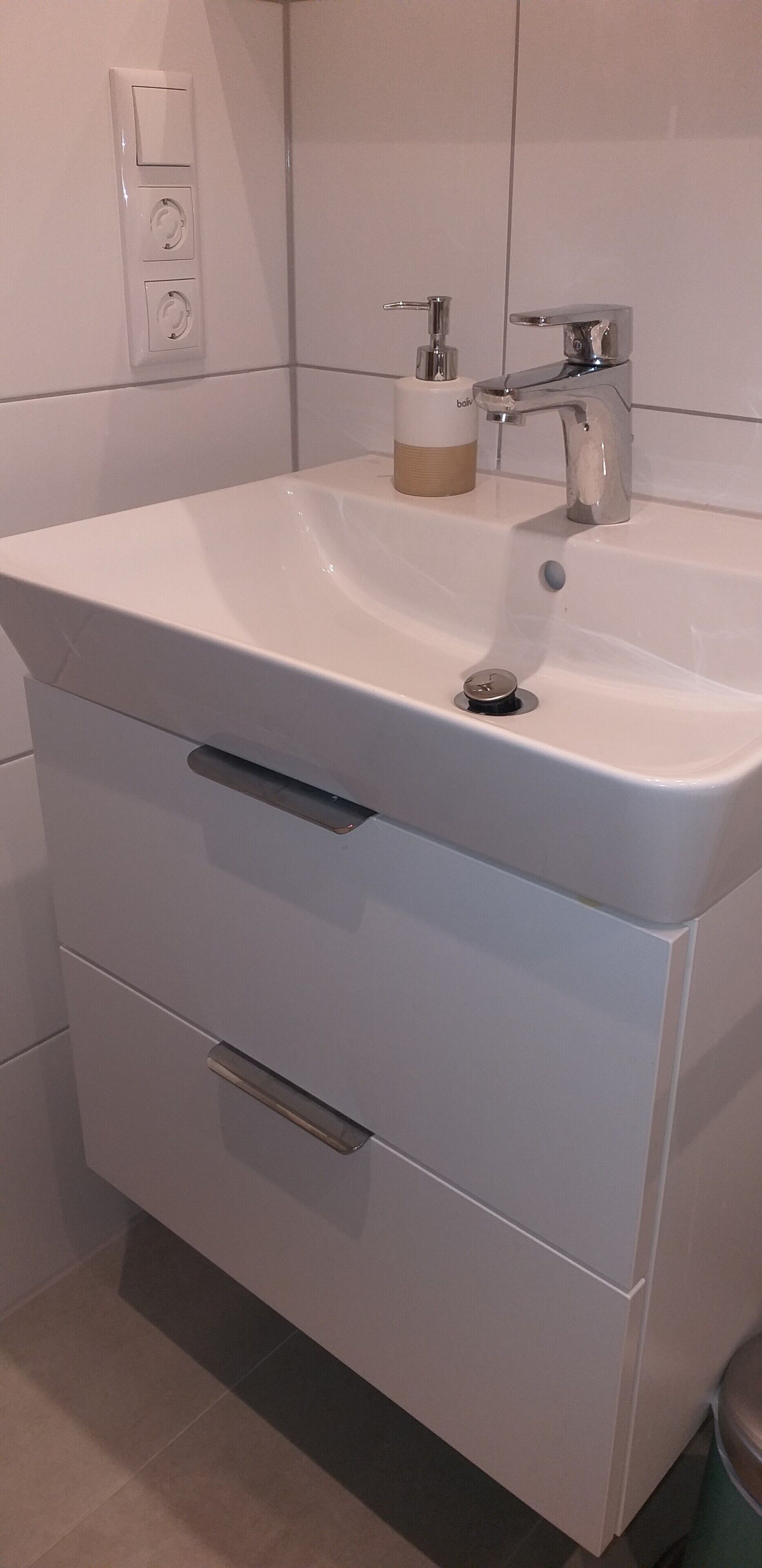 Un baño con lavamanos blanco, dispensador de jabón, grifo y retrete.