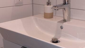 Un baño con lavamanos blanco, dispensador de jabón, grifo y retrete.