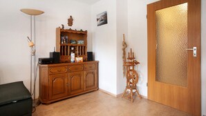 Habitació amb un armari de fusta, un filadora, una porta amb un panell de vidre rugós i una làmpada de peu.