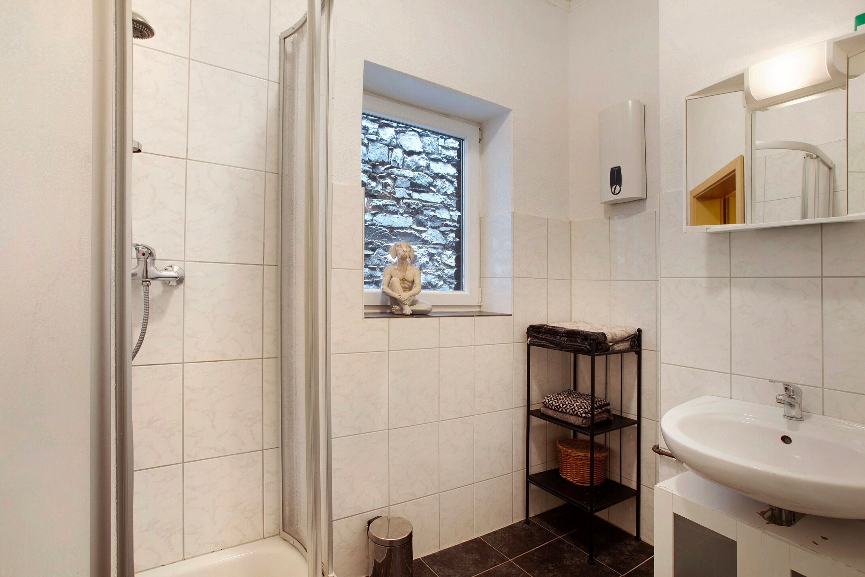 Een badkamer met een douche, een raam met uitzicht op stenen en een wastafel, plus een plank met handdoeken.
