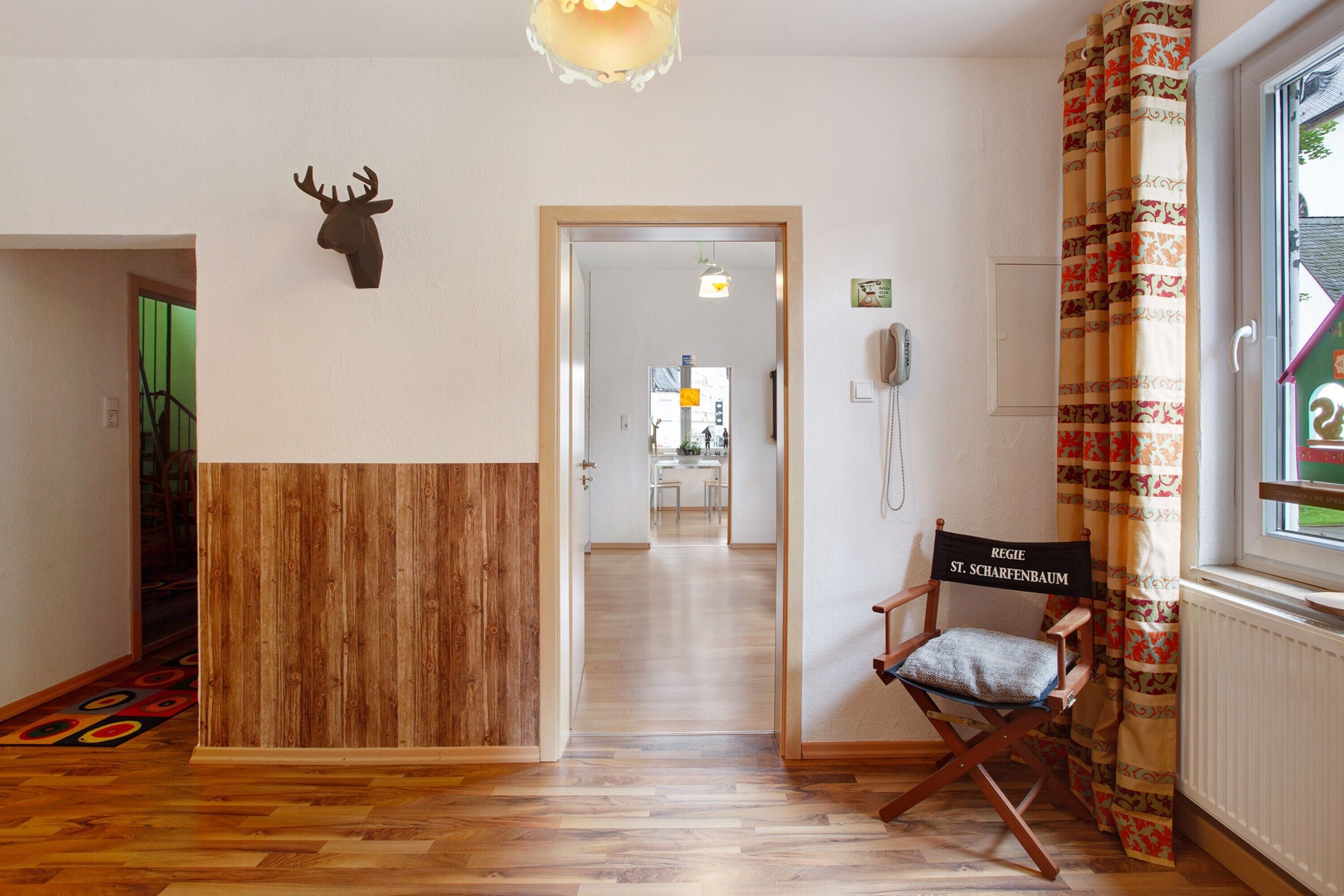 Een hotel lobby met een houten receptiebalie, een decoratie van een hertshoofd, een regisseursstoel, een telefoon en een gordijn met een patroon.