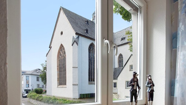 Una ventana con vistas a una iglesia y dos figuras en un estante.