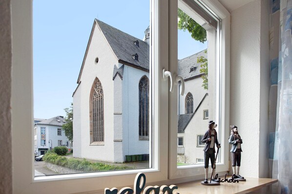 Une fenêtre donnant sur une église et deux statuettes posées sur une étagère.