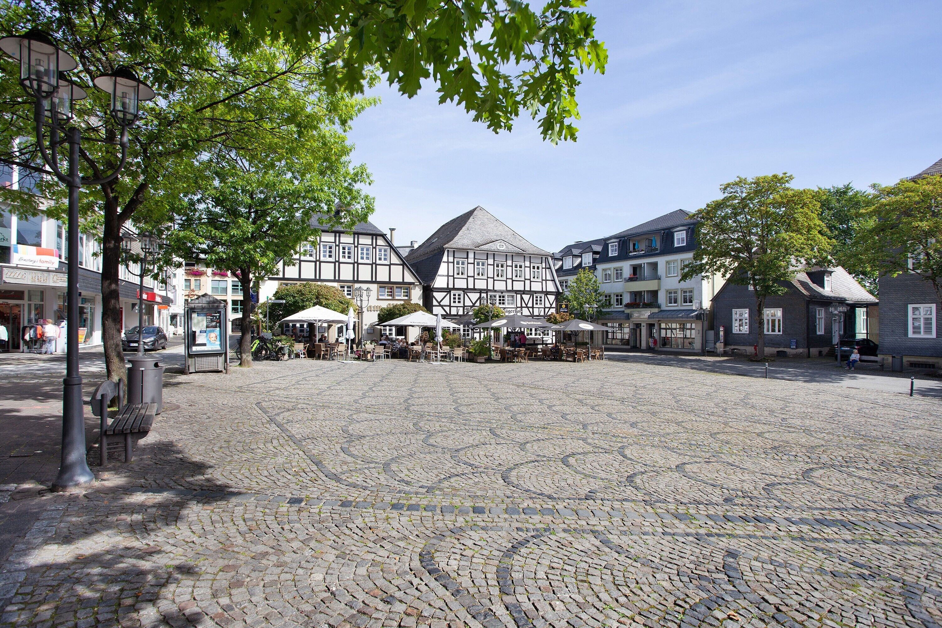 A cobblestone square with traditional half-timbered buildings, benches, and outdoor seating areas.