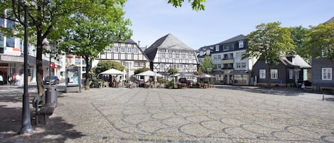 A cobblestone square with traditional half-timbered buildings, benches, and outdoor seating areas.