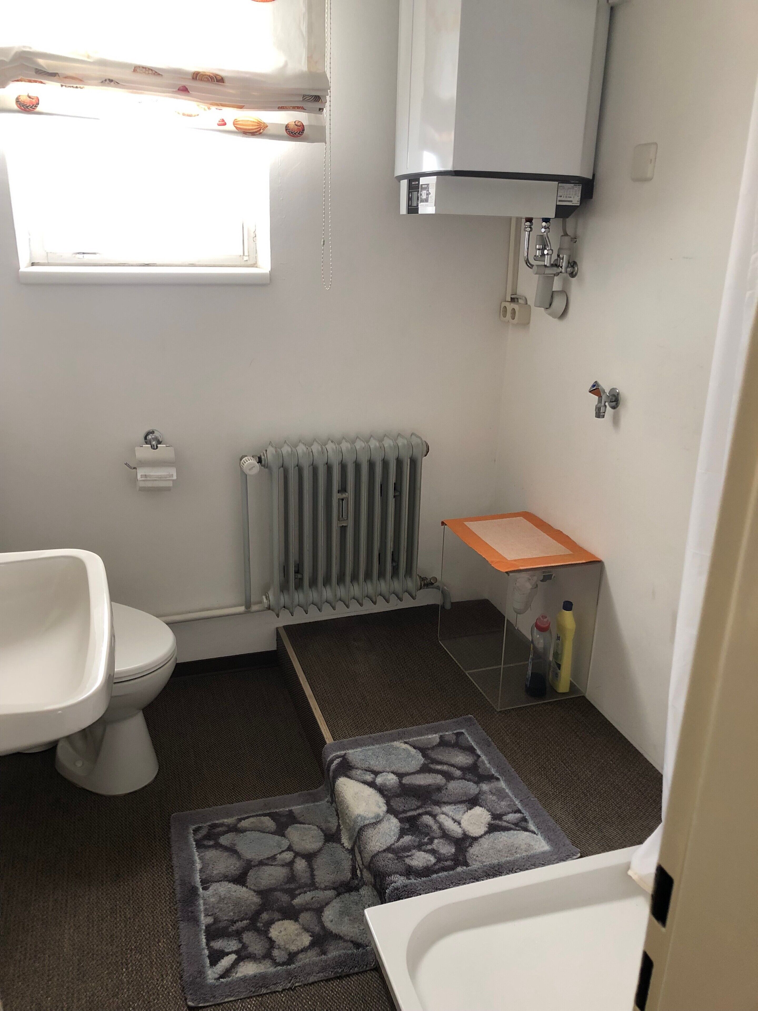 Un baño con inodoro, radiador, lavamanos y un ventanal pequeño.