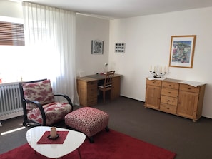 A room with a dining table, a chair, a small table with a red rug, a wooden cabinet, and a radiator. - Apartment "Innenstadt" (Marktbreit)