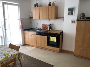 A kitchen with wooden cabinets, a black stove, and a sink. - Apartment "Innenstadt" (Marktbreit)