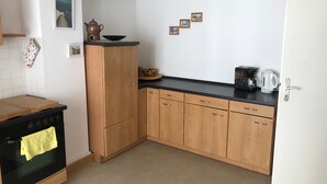Une cuisine avec des meubles de rangement en bois, une cuisinière noire et une machine à café posée sur le plan de travail.