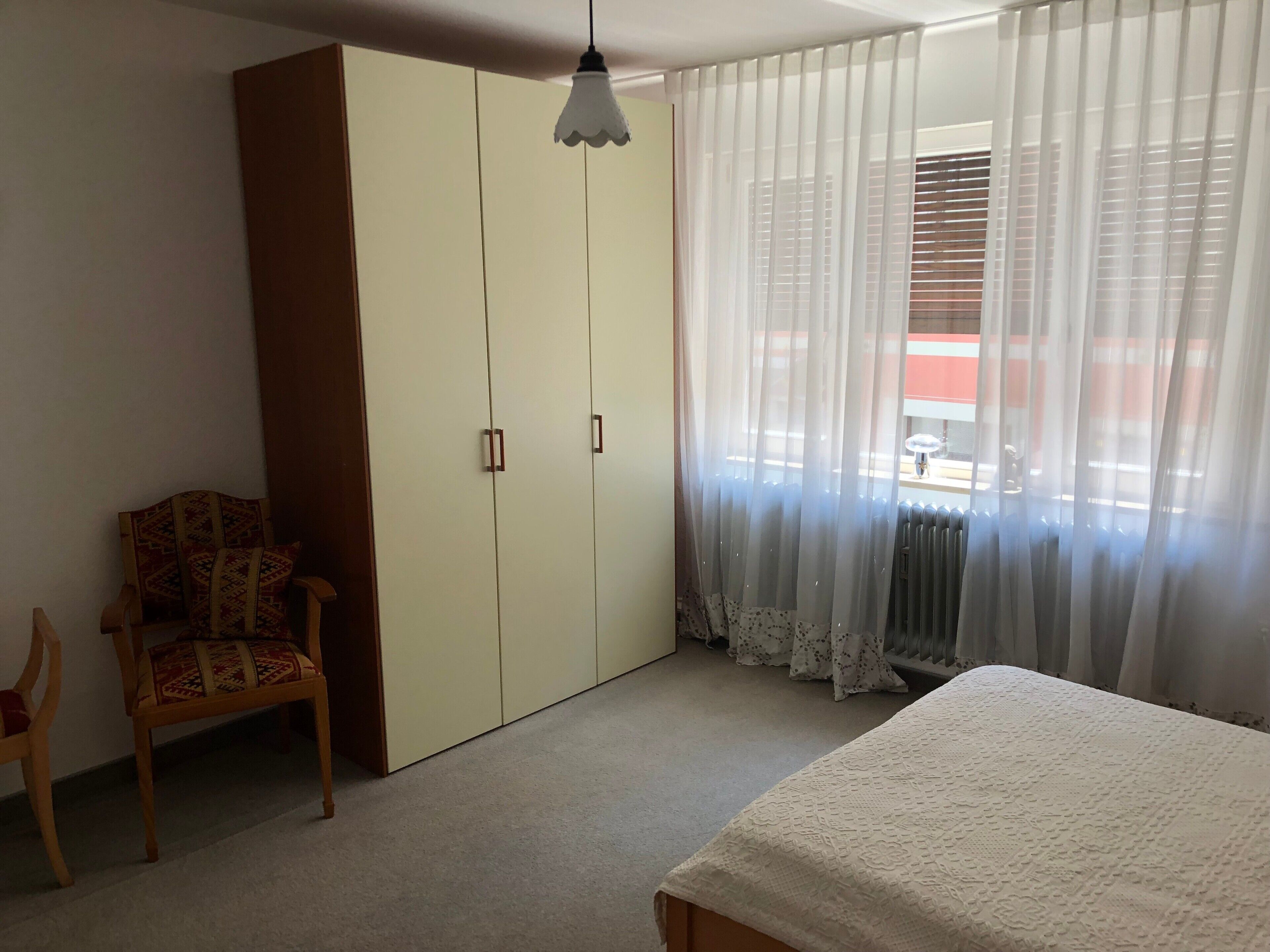 Een slaapkamer met een bed, een kledingkast, een stoel en een raam met gordijnen.