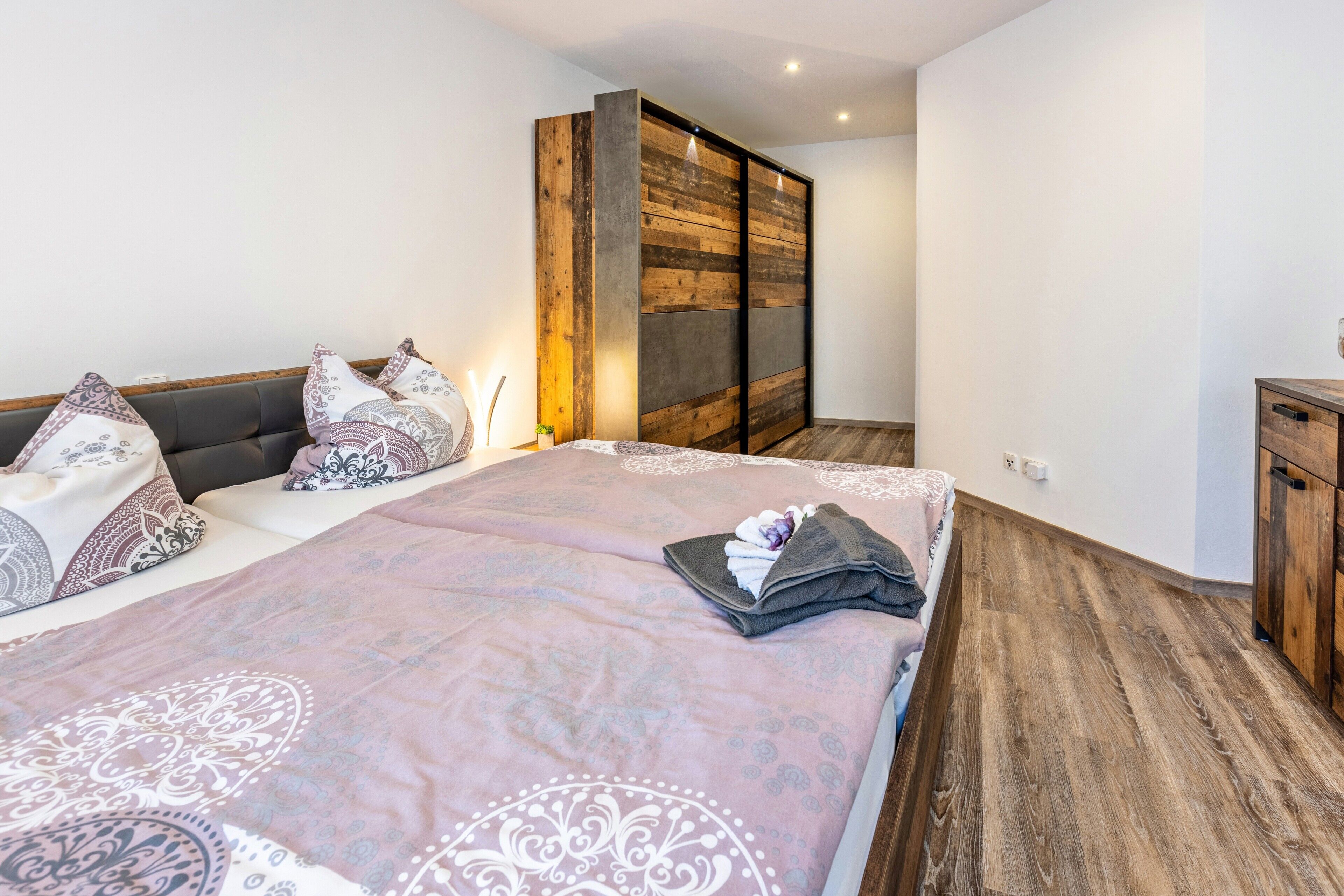 Een slaapkamer met een bed, kussens, een houten garderobe en een nachtkastje.