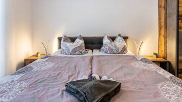 A neatly made bed with patterned bedding, two bedside tables with small plants, and a wooden headboard.
