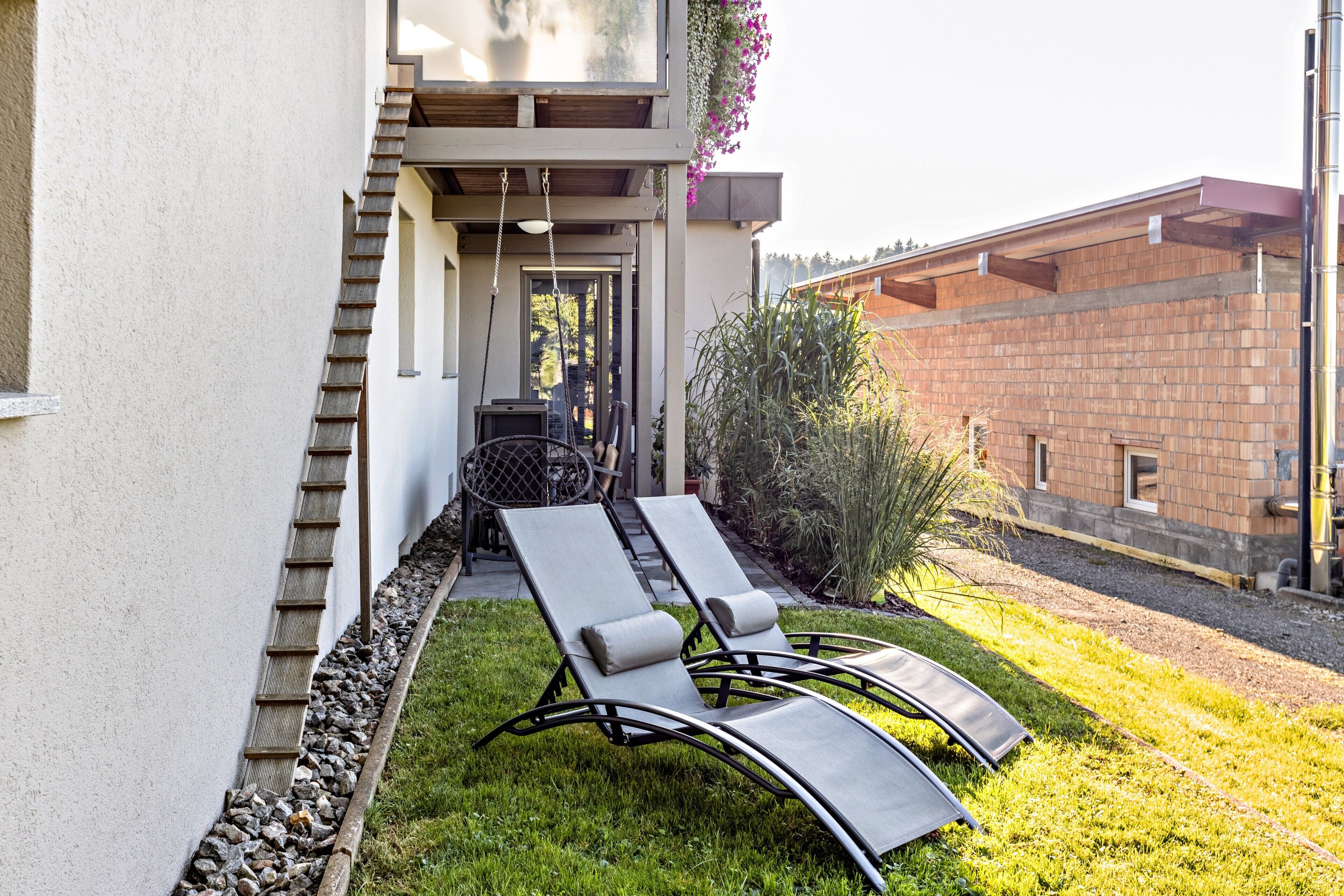 A modern outdoor seating area with two lounge chairs, a table, and a staircase leading to a covered entrance.
