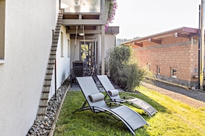 Een modern buitenverblijf met twee loungesteunen, een tafel en een trap die naar een overdekte entree leidt.