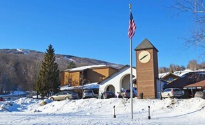A building with a clock tower, parked cars, and an American flag. - OKEMO WINTERPLACE Best Location, Ski-In/Ski-Out 4BR/3BATH + LOFT.  Spacious. (Ludlow)