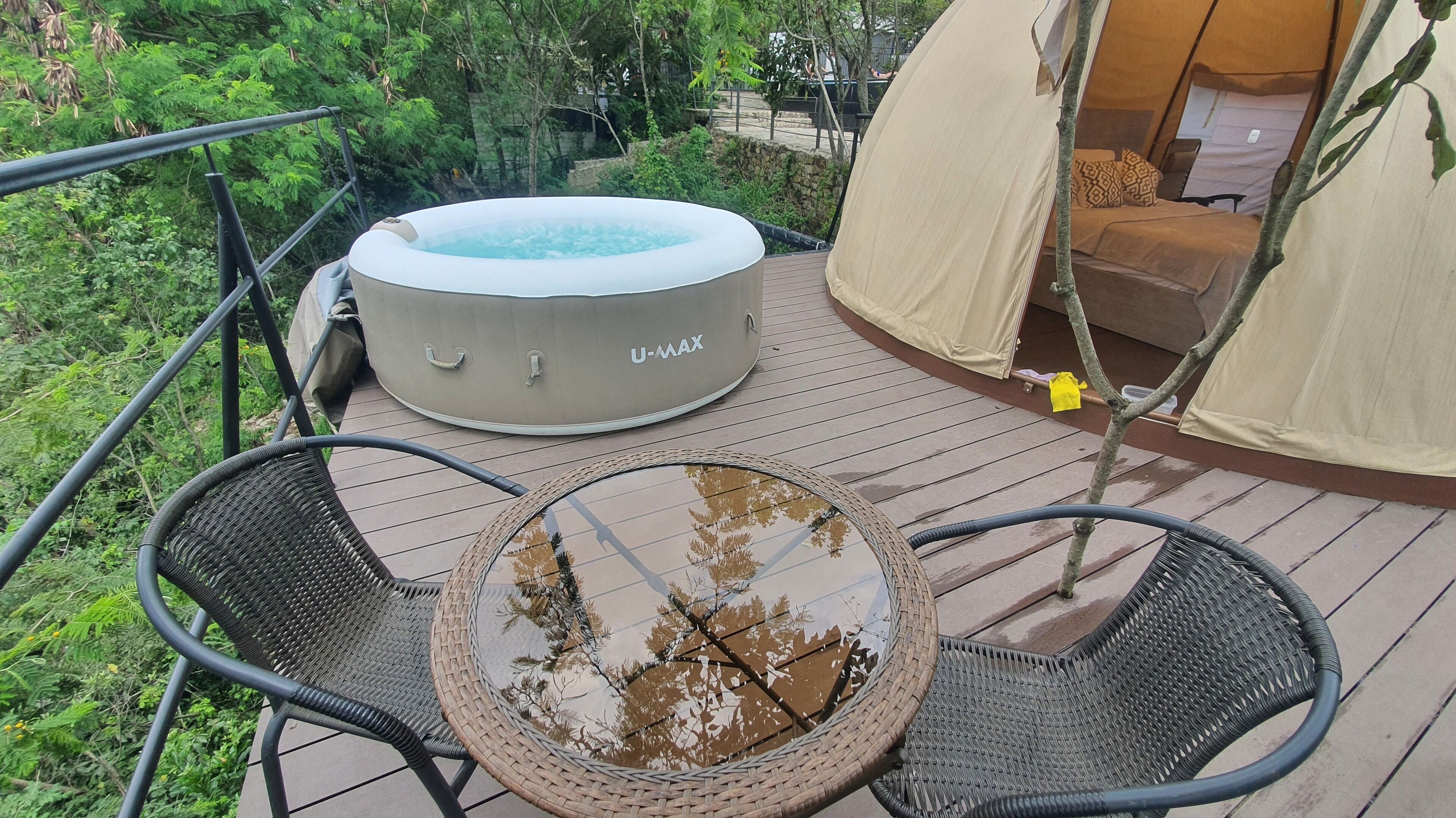 Ein Whirlpool mit der Aufschrift 'U-MAX' auf einer Holzterrasse, mit Korbstühlen und einem Glastisch.