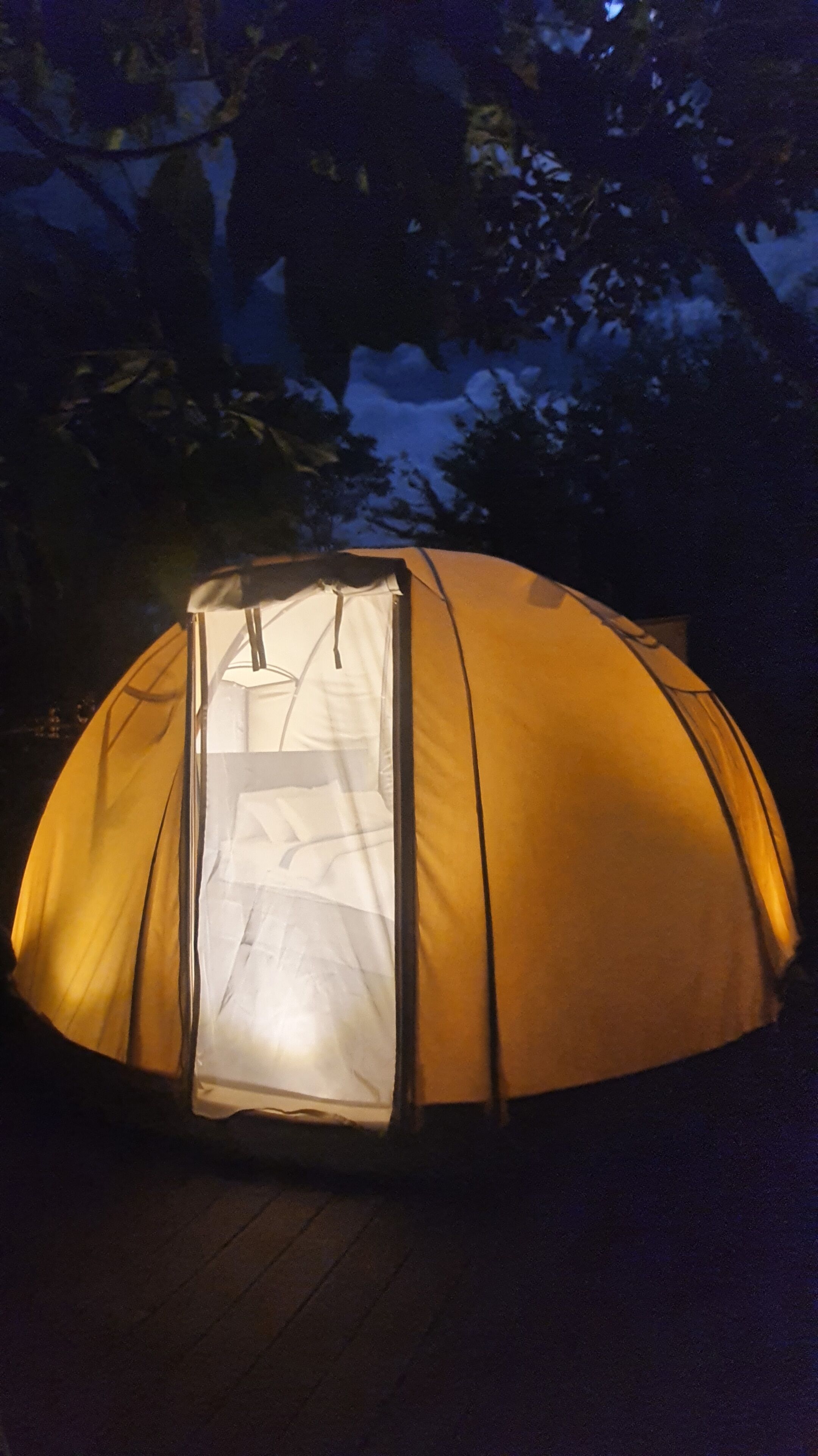 Una tienda en forma de cúpula con entrada transparente, ubicada sobre una terraza de madera.
