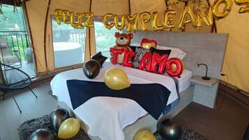 A tented room with a bed, balloons, and a 'Feliz Cumpleaños' sign.