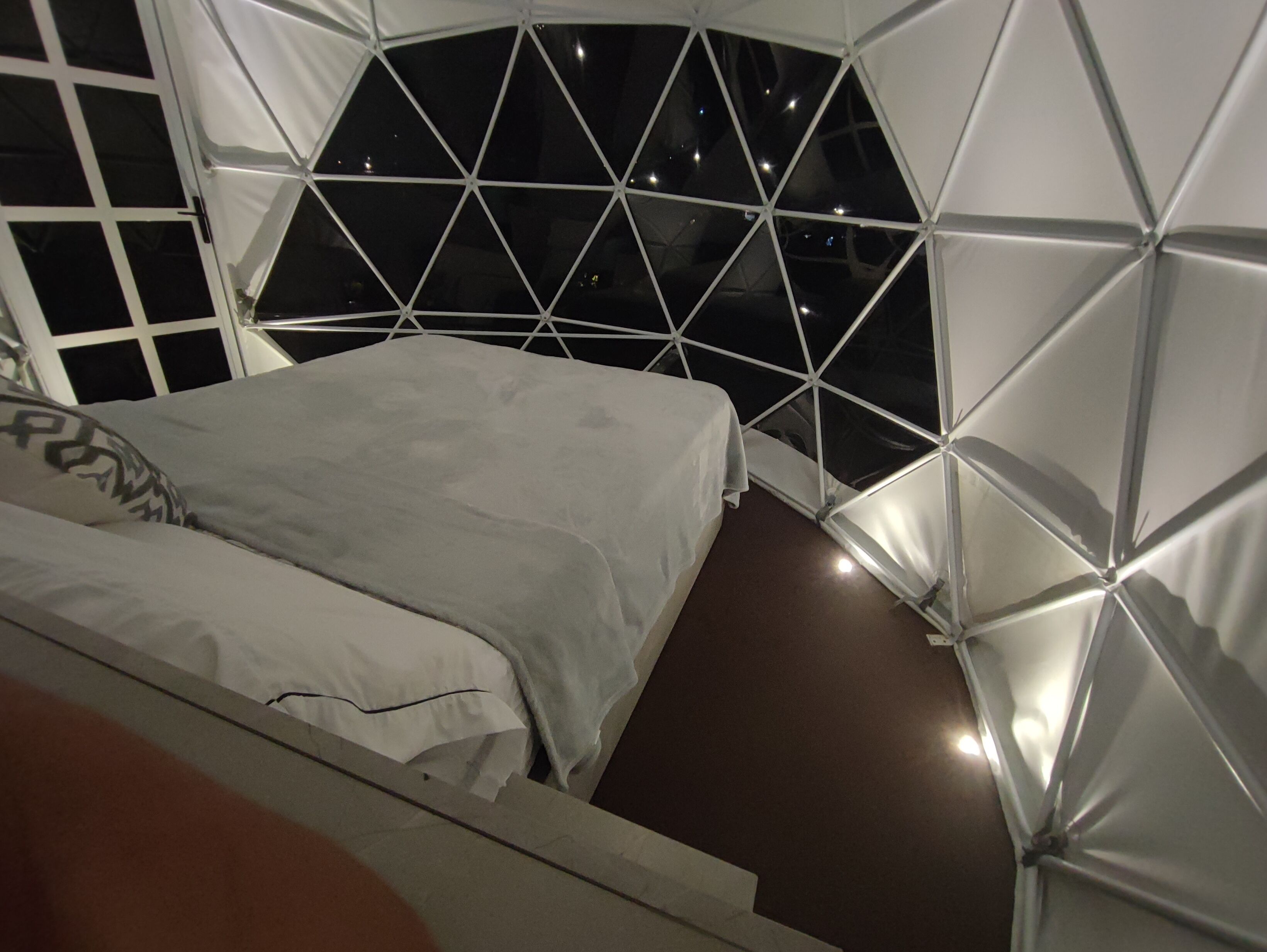A room with a bed, a window, and a view of the night sky.