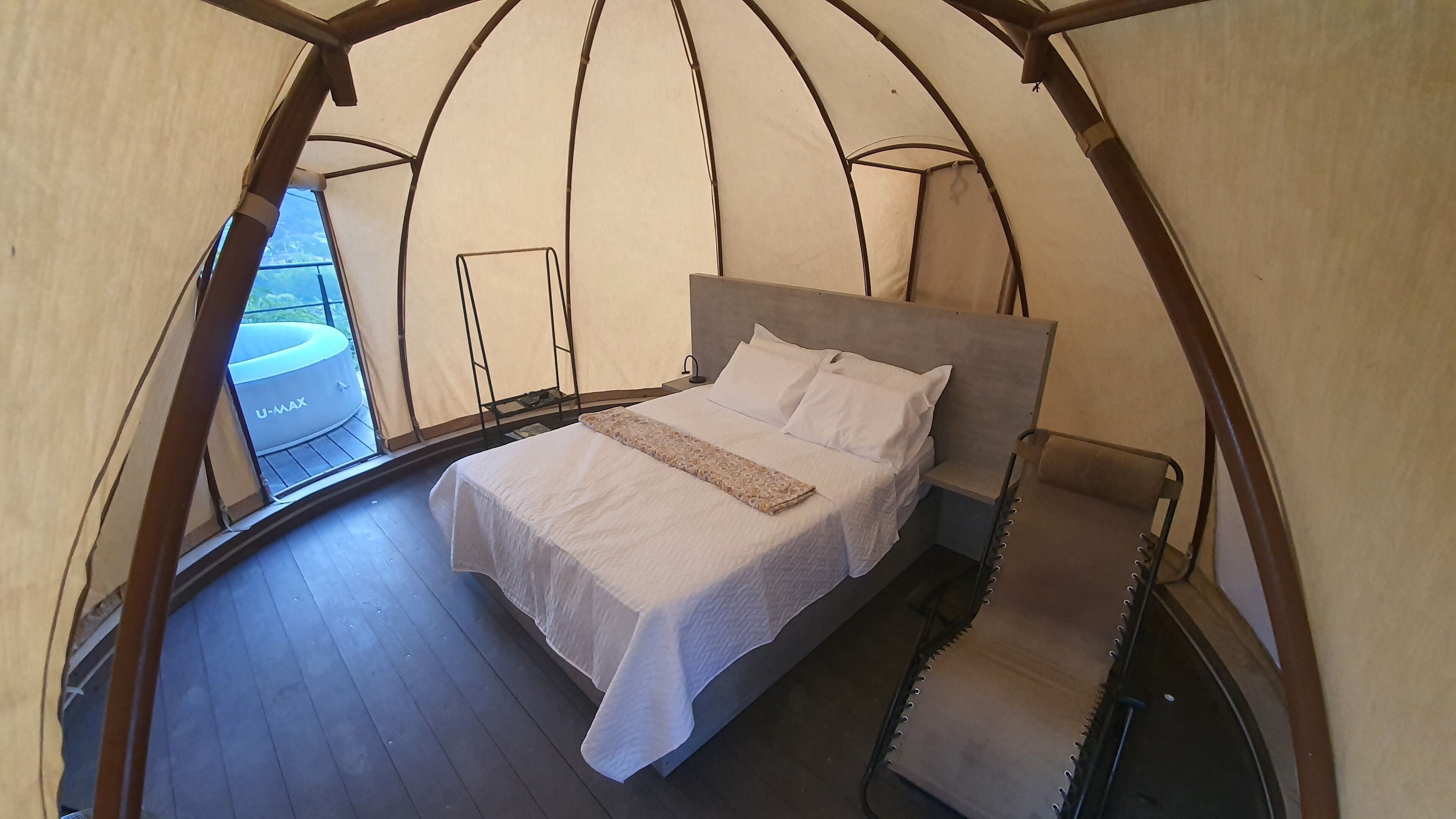 Habitación tipo tienda de campaña con cama, una silla y vista a un vehículo U-MAX afuera.