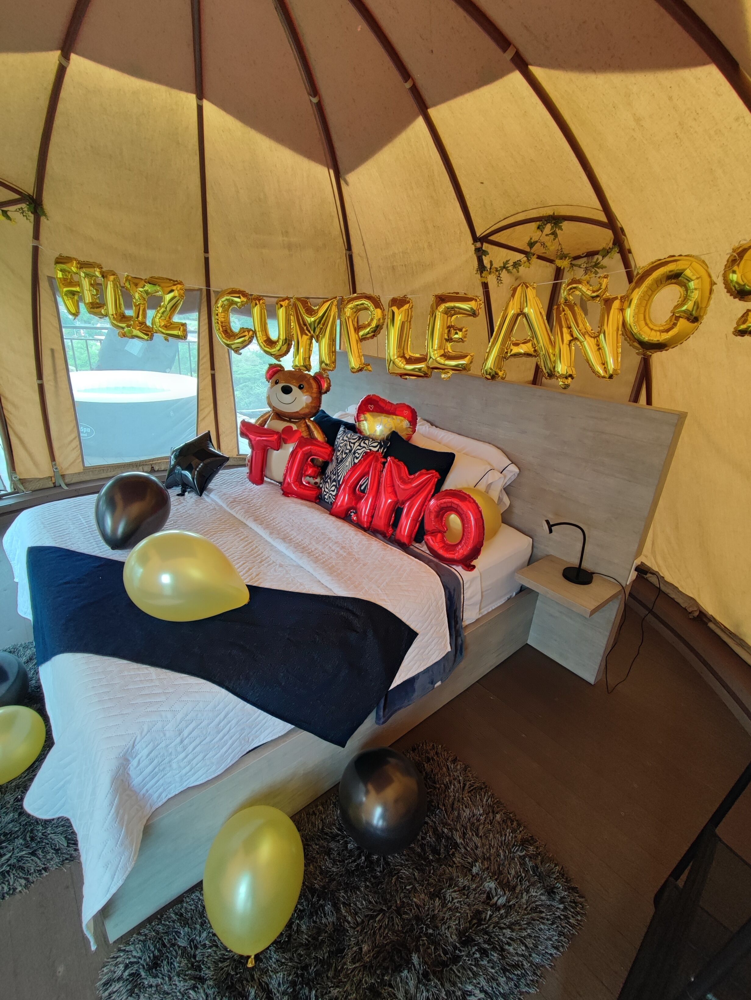 A tented room with a bed, balloons, and 'Feliz Cumple Anno' decorations.