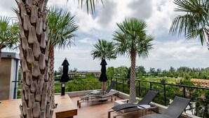 A rooftop terrace with lounge chairs, palm trees, and a view of the landscape. - Citygate Kamala Residence P506  (Kamala)