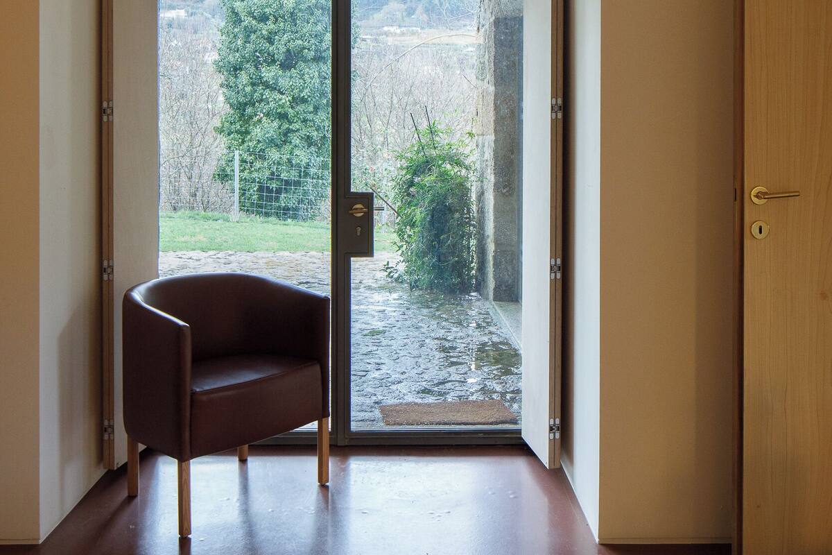 Une pièce dotée d’une porte-fenêtre coulissante donnant sur un jardin, d’un fauteuil marron et d’une porte en bois.
