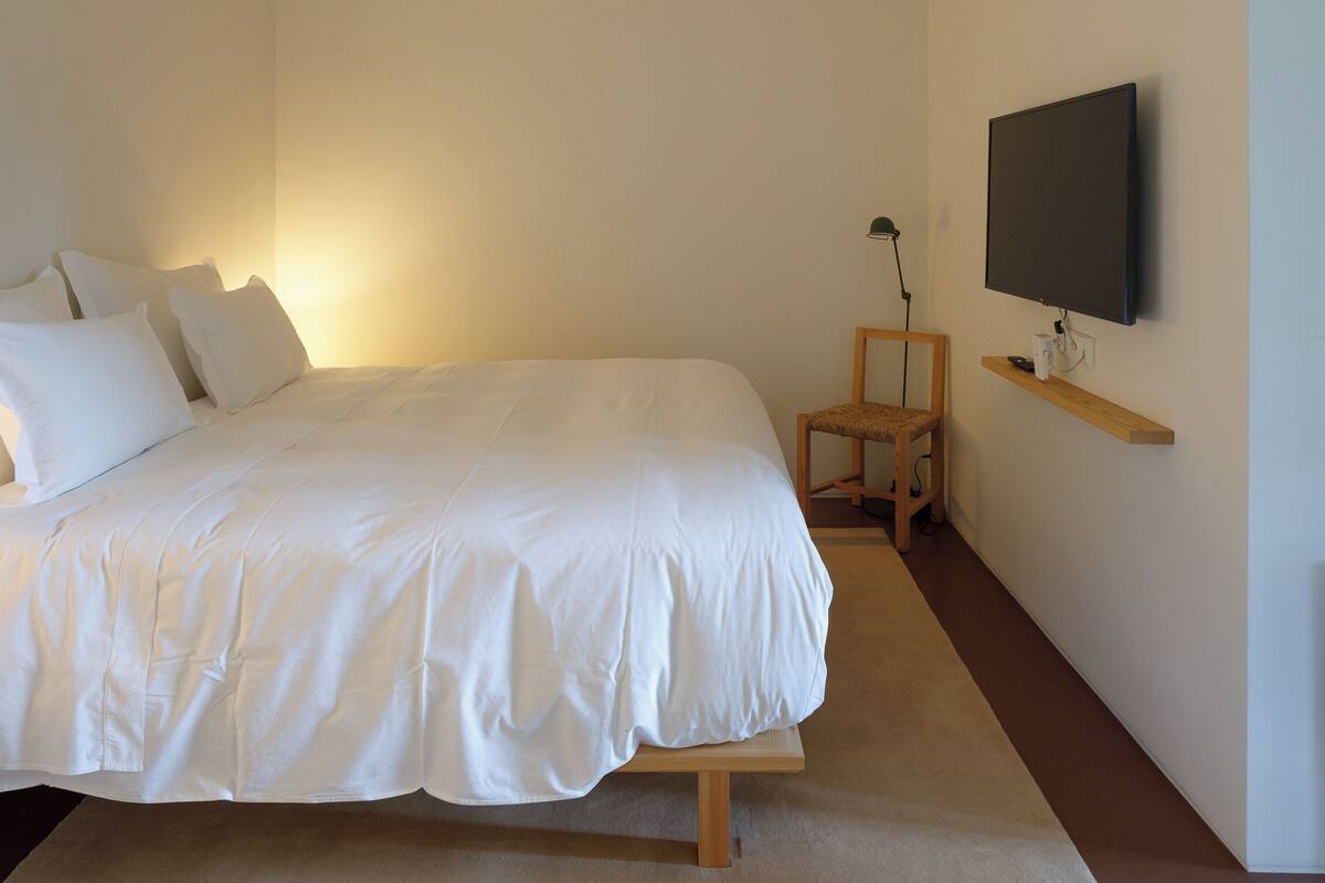 Une chambre à coucher avec un lit, une chaise, un téléviseur fixé au mur et une table de chevet.