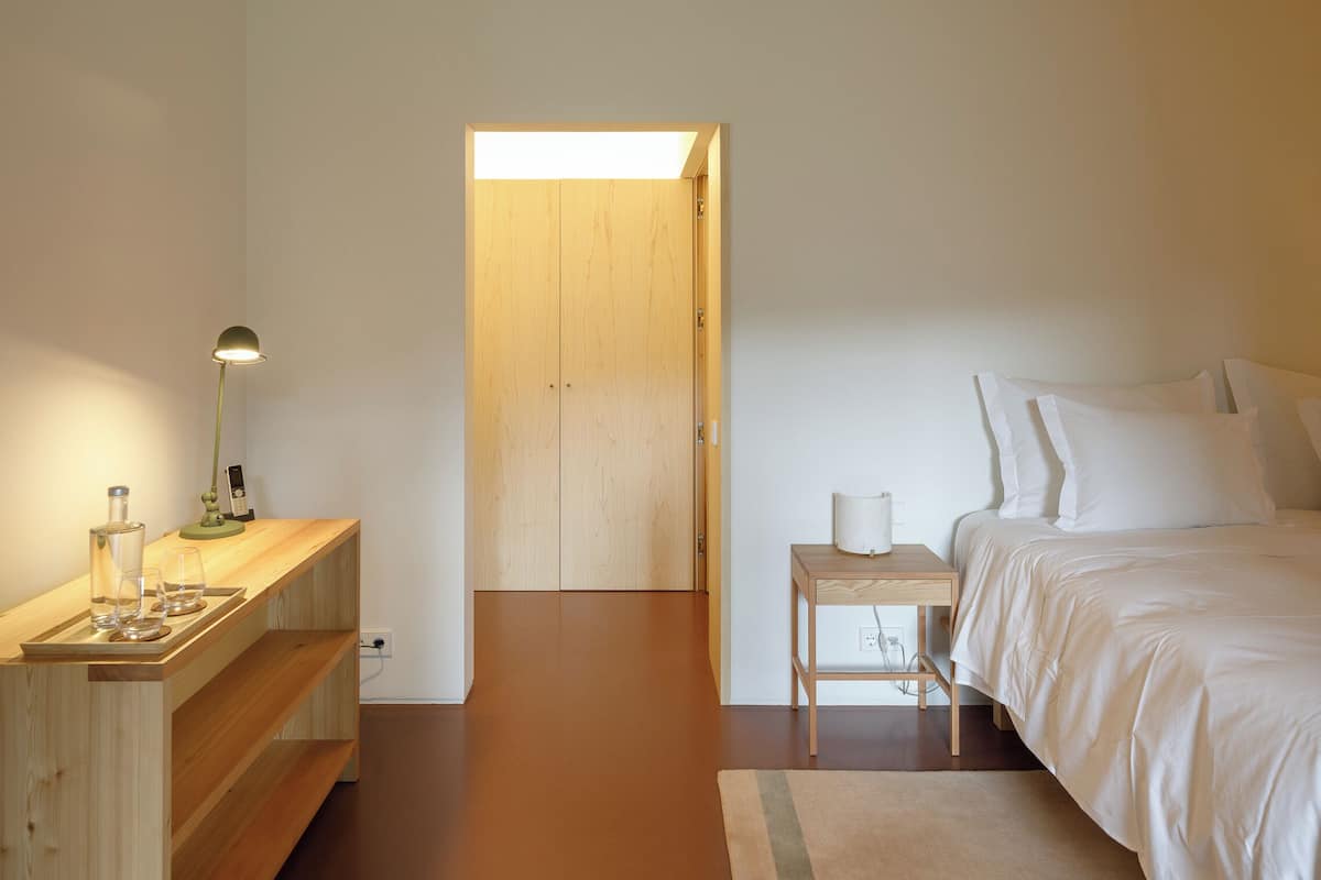 Une chambre à coucher au style minimaliste, avec une armoire en bois, une table de chevet et un lit recouvert de linge de lit blanc.