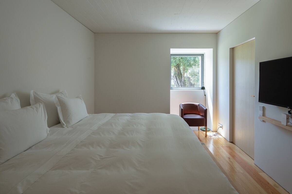 Une chambre avec un grand lit, une chaise, une télévision et une fenêtre donnant sur des arbres.