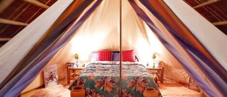 A tent with a bed, pillows, a table, and a vase.