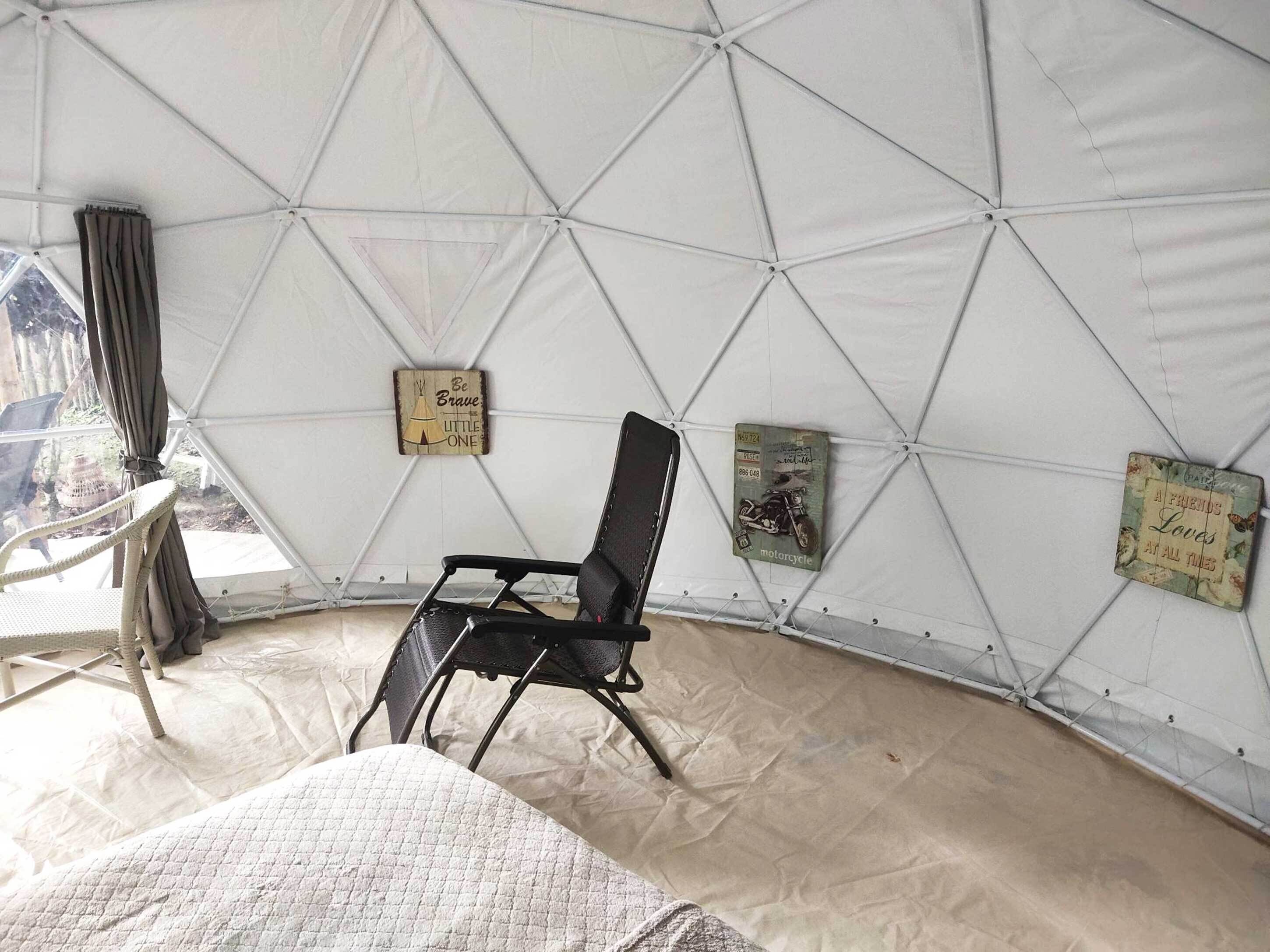 A tented room with a black chair, a quilted bed, and wall decorations including a 'Be Brave' sign and a 'A Friend's Love' sign.