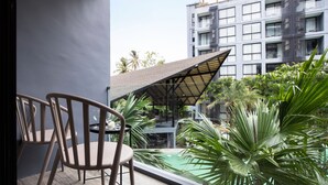 A balcony with two chairs, a table, and a view of a swimming pool and a building with multiple balconies. - Citygate Kamala Residence P204 (Kamala)