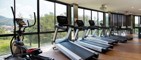 A gym with treadmills and an elliptical machine, large windows, and a view of greenery.