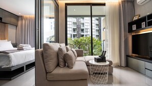 A modern hotel room with a bed, sofa, TV, and a balcony with plants. - Citygate Kamala Residence P204 (Kamala)
